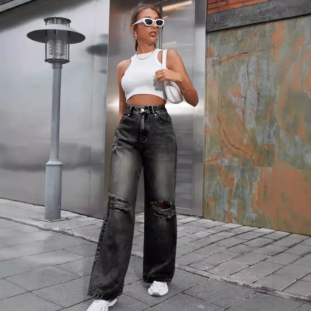 Woman wearing ripped high waist wide leg jeans and a white crop top, posing stylishly outdoors.