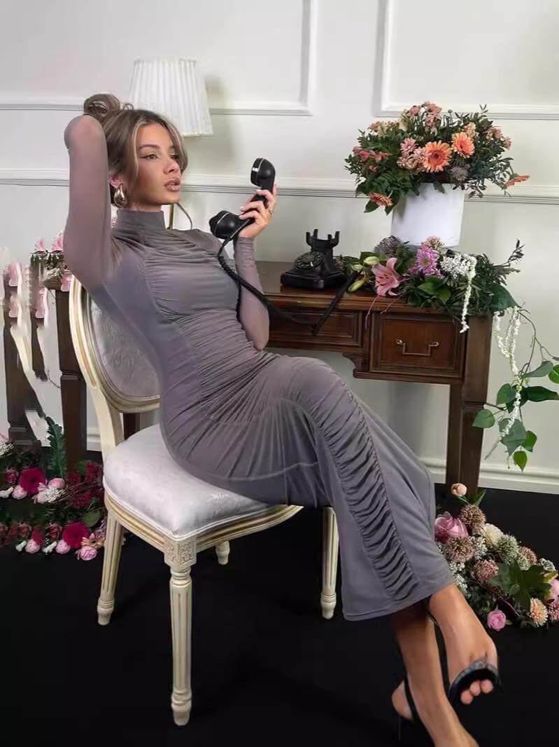 Model wearing a pleated high collar slim dress while sitting at a desk with a vintage telephone.