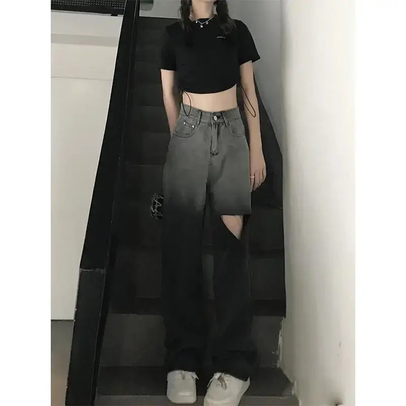 High waist ripped jeans for women shown on a model wearing a black crop top and sneakers, standing on stairs.